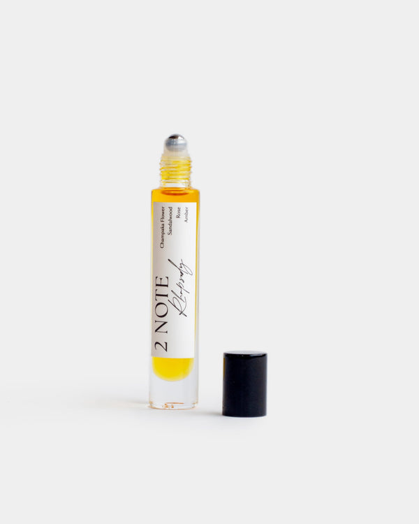 Rhapsody in tall clear glass roller bottle — botanical fragrance oil, warm amber, uncapped