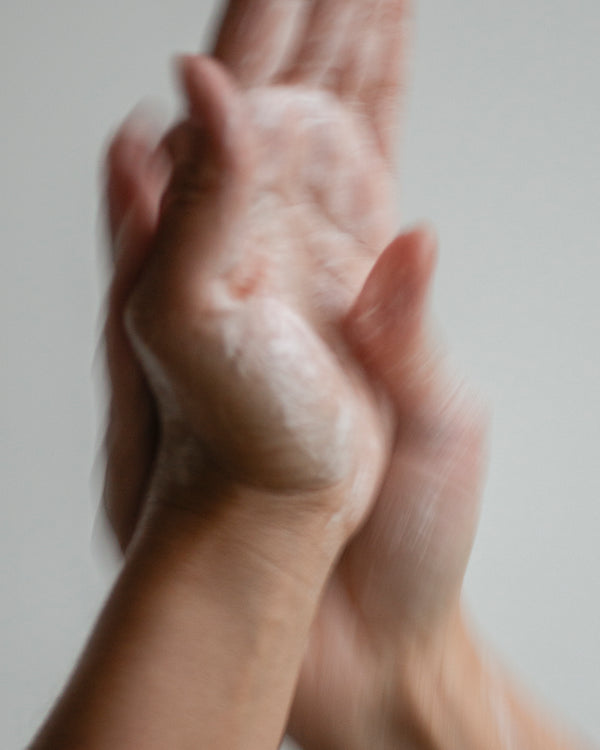 Hands of queer nonbinary model with light olive complexion lathering with botanical skincare Hand Soap foam — natural skincare hand wash in use, motion blur on soft gray