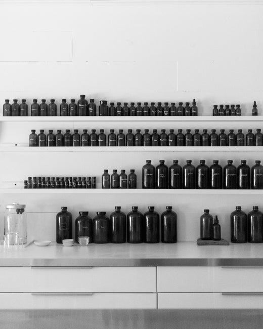 Carolyn Mix and Darcy Doniger, founders of 2 Note: Botanical Fragrance & Skincare, stand together in their studio workshop, surrounded by brown glass containers filled with essential oils, absolutes, resins, tinctures, botanical extracts, and product formulas.